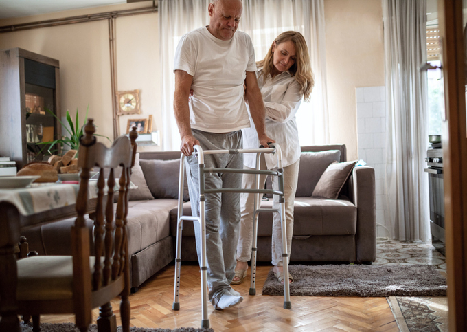 Caregiver helping a man walk using a walker.