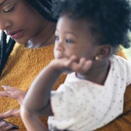 Mother holding toddler and using smartphone.