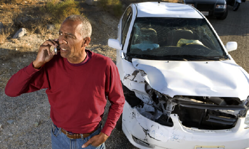 A man calls his insurer about his totaled vehicle sitting in the background