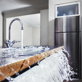 Running kitchen faucet is overflowing with water that is spilling over the counter
