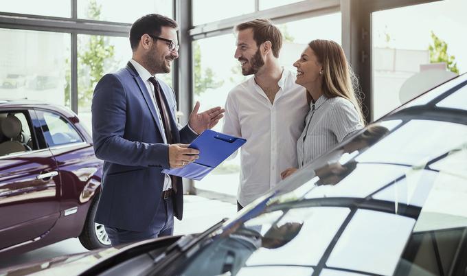Car salesman talking to a couple in car showroom.