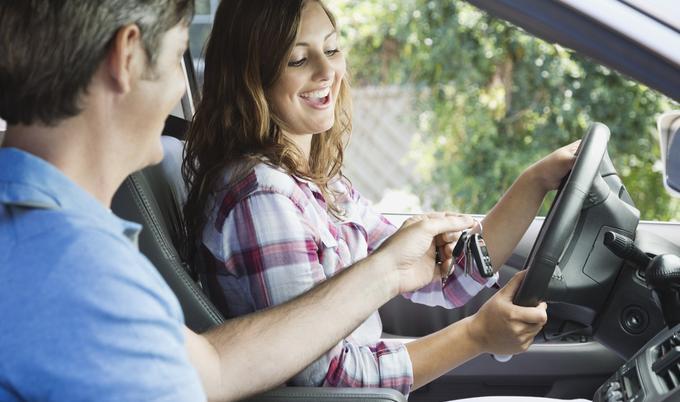 Father handing car keys to daughter in driver's seat. 