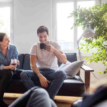 Couple sitting on couch, drinking coffe and smiling.