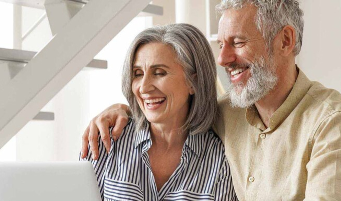 A happy couple sitting on a couch looking at a laptop. 