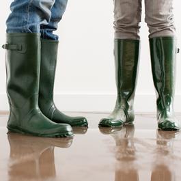 Two people wearing rubber boots while standing in floodwater.
