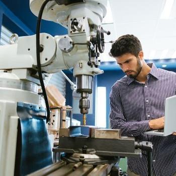 A man on laptop calibrating a large drill.