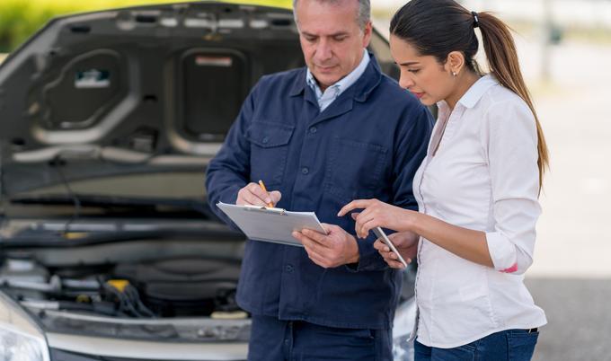 Woman talking to mechanic in front of a car.
