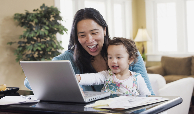 Mother holding baby and smiling while looking at laptop
