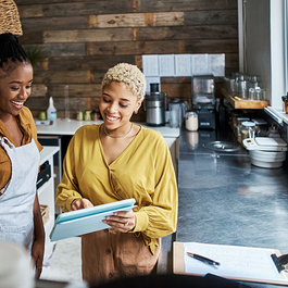 A cook and manager standing in a commercial kitchen looking at a tablet smiling.