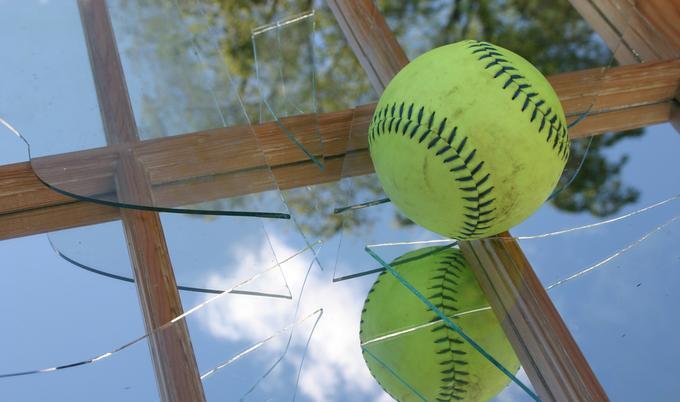 Baseball sitting on cracked glass from a broken window.