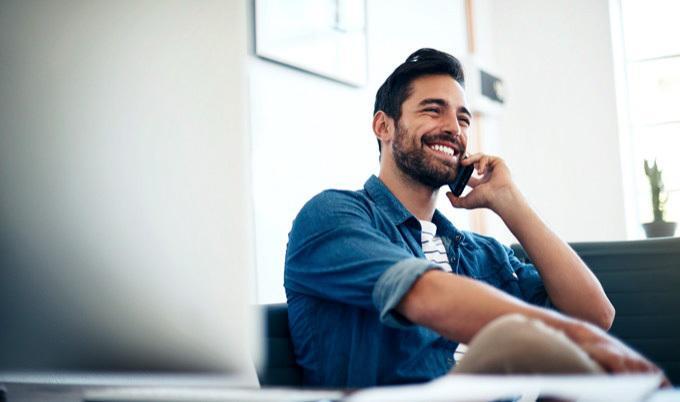Smiling man in denim shirt is talking on mobile phone, sitting down.