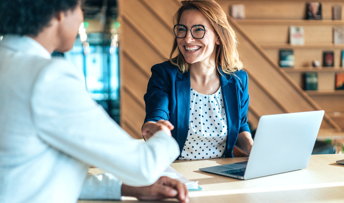 Two women shaking hands at a desk.