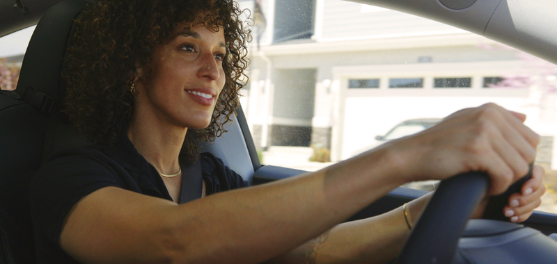 A multiracial woman driving a car in a suburban residential area.