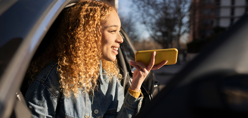 A woman gets out of her car holding a yellow phone