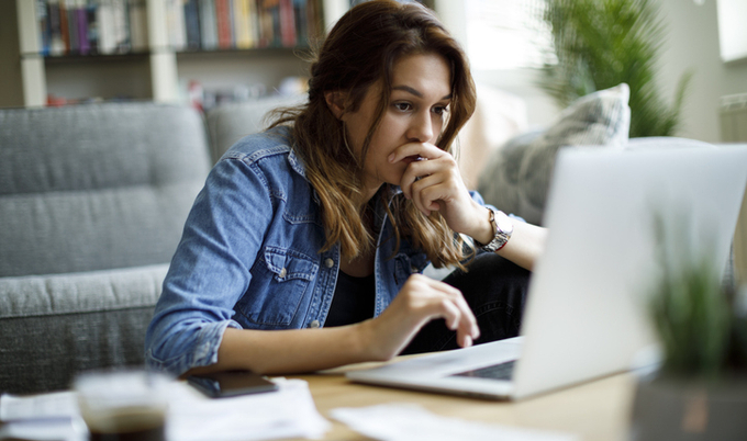 Woman sitting in front of a laptop in thought at a coffee table.