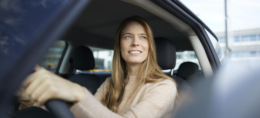 Smiling woman sitting in the driver's seat of a car with her hand on the wheel.