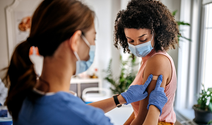 Nurse placing a bandaid on the are of a patient in a mask.