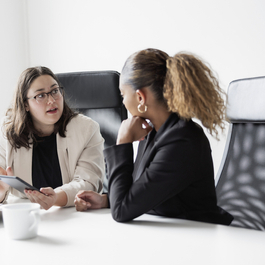 Two female professionals having a discussion in an office setting.
