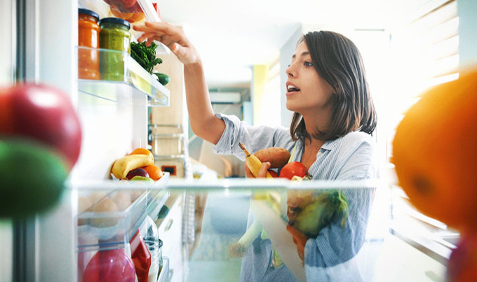 Woman grabbing vegetables out of the fridge.