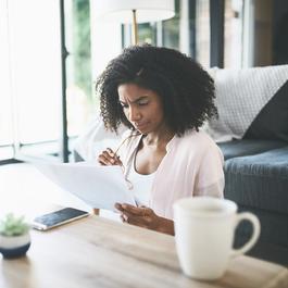 Woman sitting on floor while reading paperwork.
