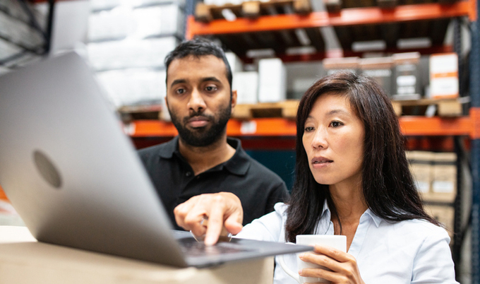 Two co-workers looking at a computer in a warehouse.
