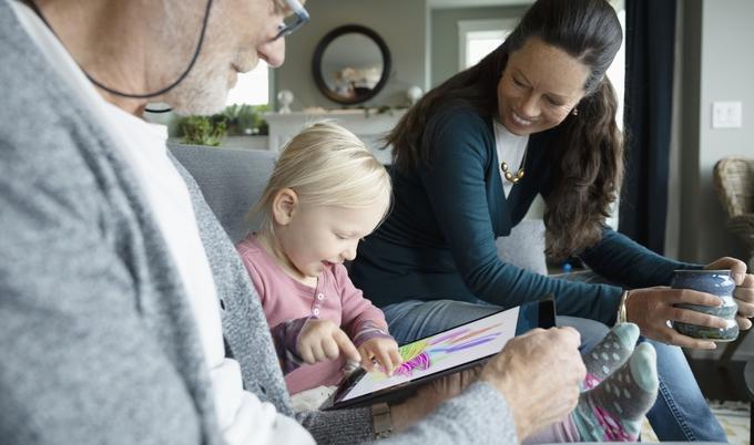 Grandparents sitting with granddaughter and drawing on a tablet.