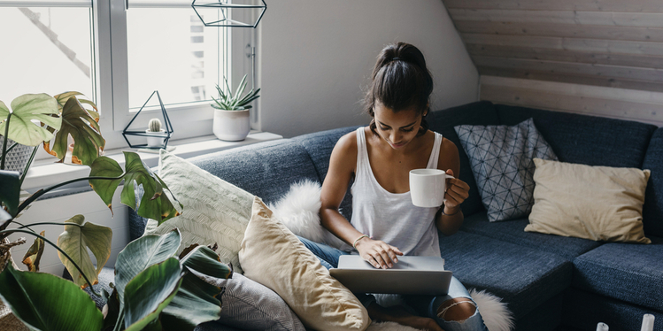Young woman sitting on the couch with cup of coffee using laptop