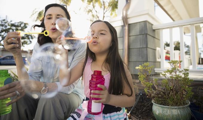 Grandmother and granddaughter outside of house blowing bubbles.