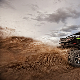 A person driving an ATV kicking up dirt behind it.