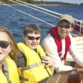 Father, son and daughter sailing on lake wearing life jackets.