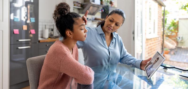 A mom feels her daughter's forehead for a fever during a telemed appointment