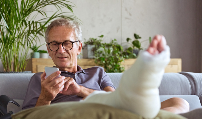 Man sitting on the couch on his phone with his leg up in a cast.