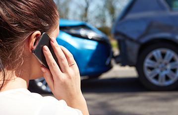 Woman on phone in front of a car accident. 