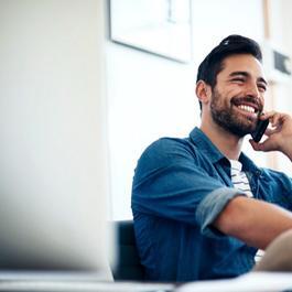 Smiling man in denim shirt is talking on mobile phone, sitting down.