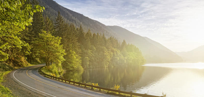 Curved road next to lake with setting sun