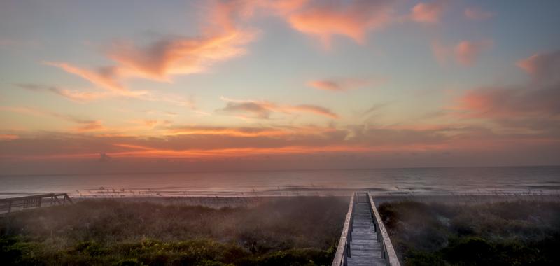 A fiery orange sunset illuminating wooden walkways leading out to a Florida beach