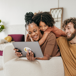 Smiling parents and young daughter looking at tablet together in living room