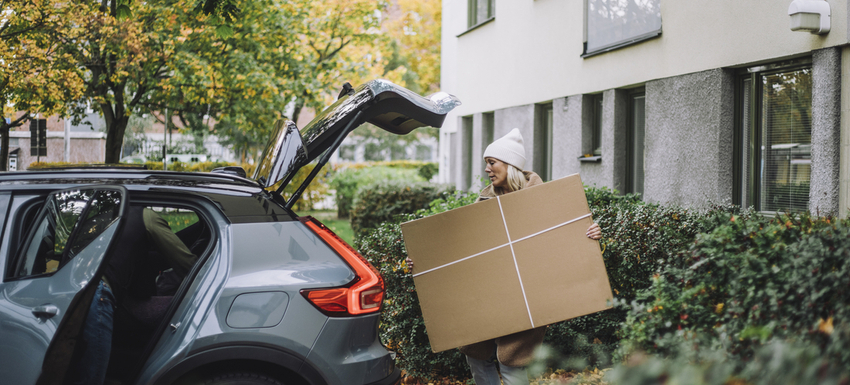 Woman walking towards car trunk carrying cardboard