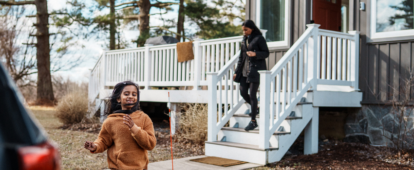 Elementary age girl smiling, running to a car to help her mom unload groceries.
