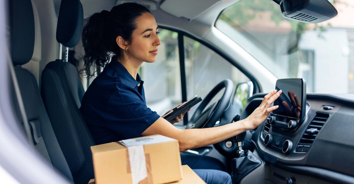 Delivery woman driving van with packages on the front seat.