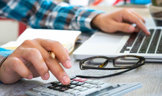 Man checking finances on calculator and laptop.
