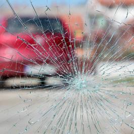 View a cracked windshield with blurred red car in the background.