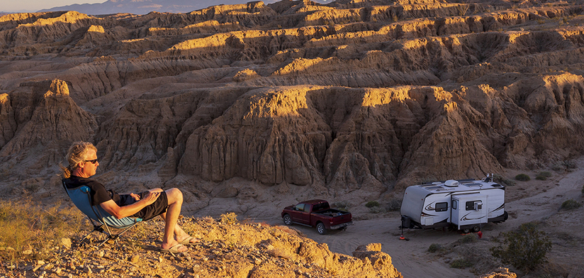 A man lounging on a hill overlooking a campsite in the desert badlands