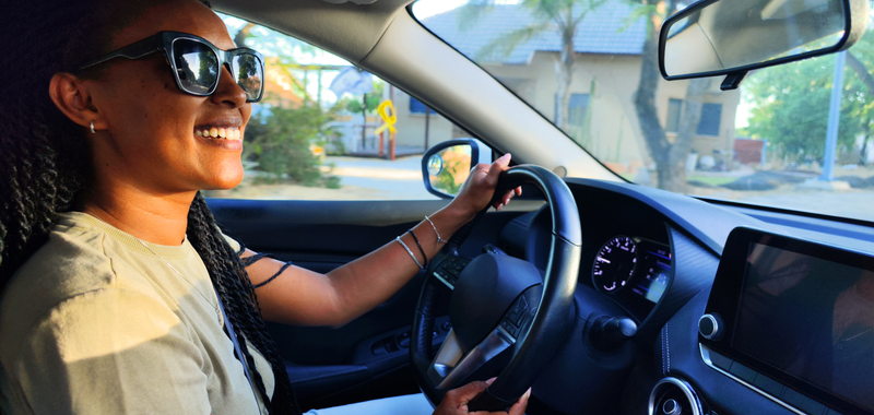 Woman sitting in her car smiling in the sunlight on the road.
