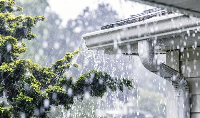 Rain falling over gutters on a house.