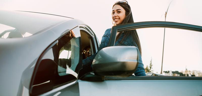 Smiling woman with sunglasses on her head entering driver's side of a car