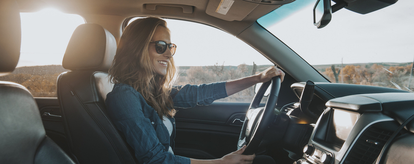 Inside view of a car, a woman is driving with sunglasses on as she looks down at the infotainment system.