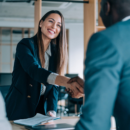 A man and woman shaking hands over a desk.