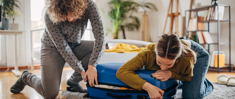 Two people packing suitcases together in bedroom, woman's suitcase is full.