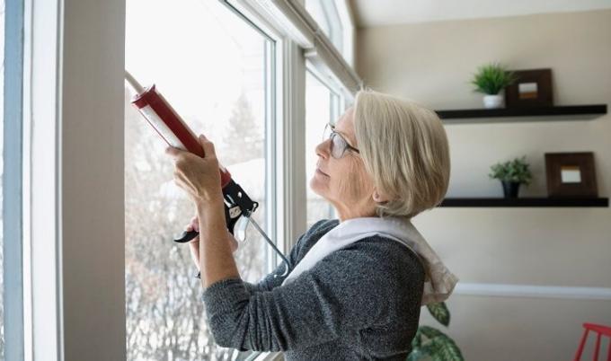 Older woman caulking windows with a caulk gun.